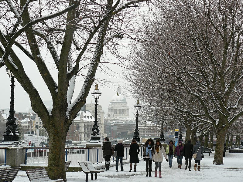 People walking along the river in London with snow everywhere and St Paul's Cathedral in the background