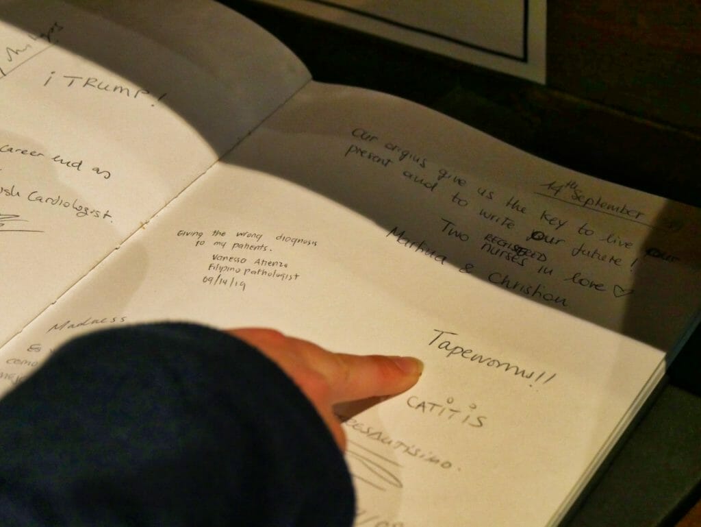 Book of Medical fears at The Old Operating Theatre, with Kalyn pointing at the word "tapeworms!"