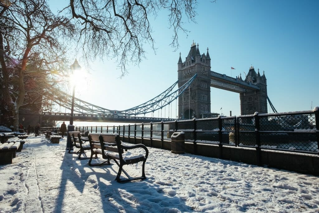 Tower Bridge, London, with blue sky behind and park benches in front, covered in snow