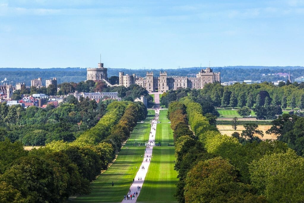 A long path leading to Windsor Castle, with people walking along it, with green grass and blue sky