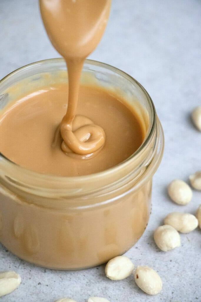 spoon with peanut butter dripping into jar of peanut butter