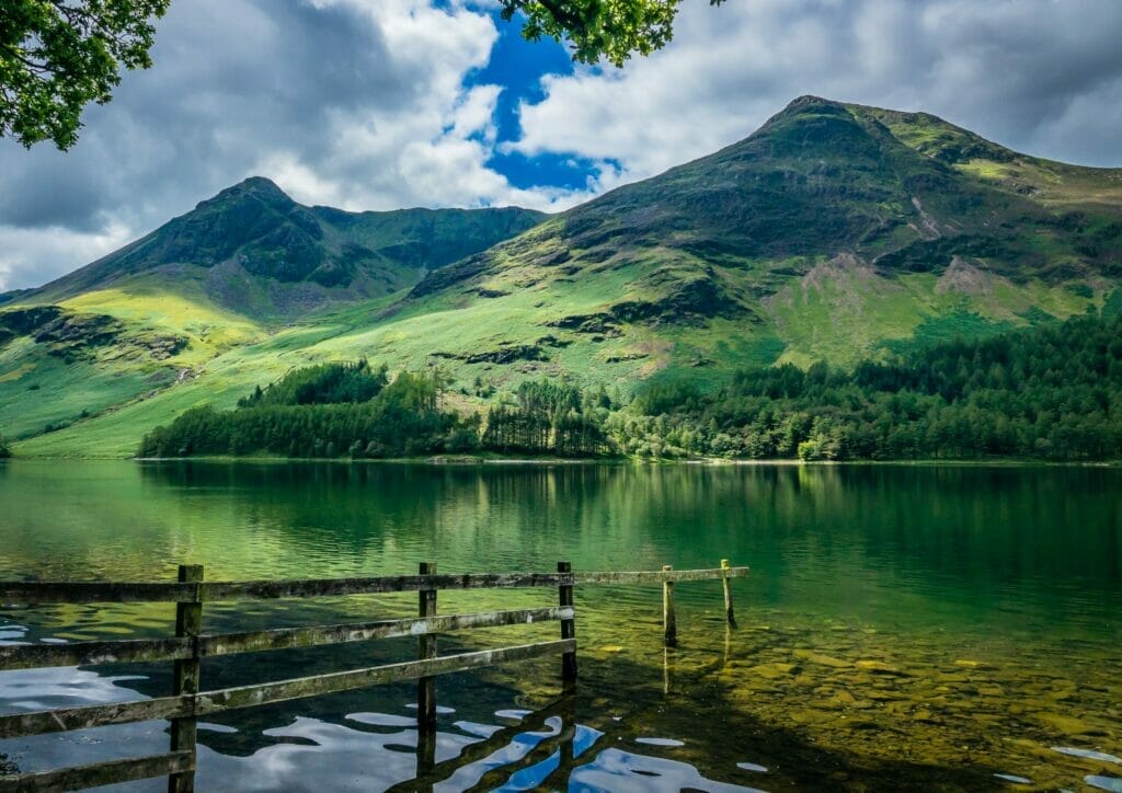 One of the lakes in the Lake District with a hill behind, covered in trees and greenery. This is one of the best views you can enjoy on a Lake District tour from London. 