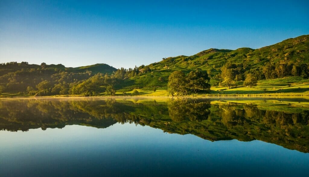 Green hills in the Lake District with a lake in the front and a blue sky overhead. 