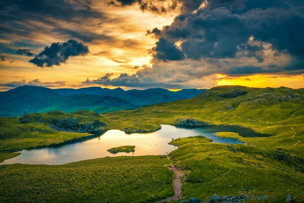 Overhead view of a lake in the Lake District, with a sunset-filled sky and some hills in the background. 